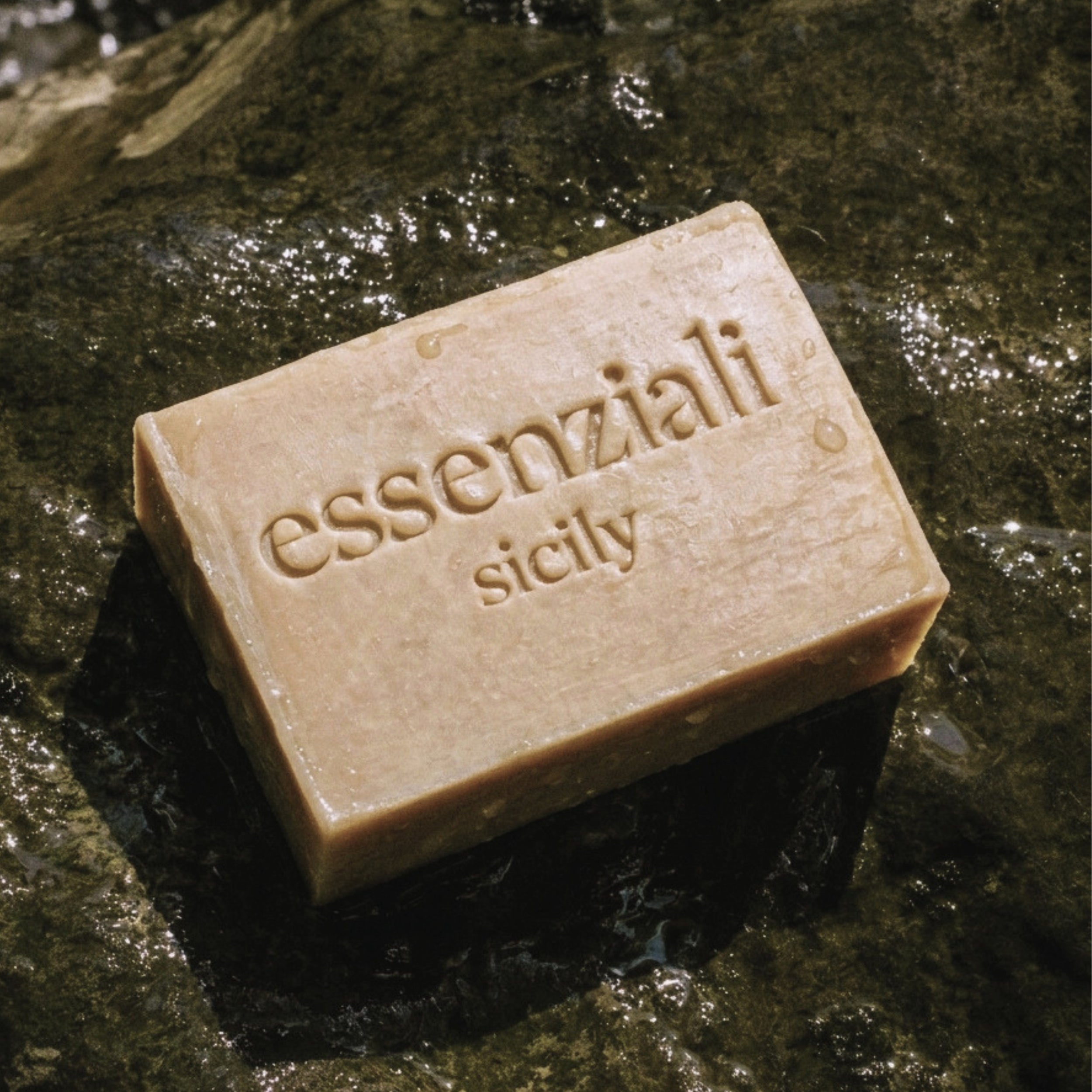 Bar of soap with 'essenziali sicily' branding on a wet stone surface