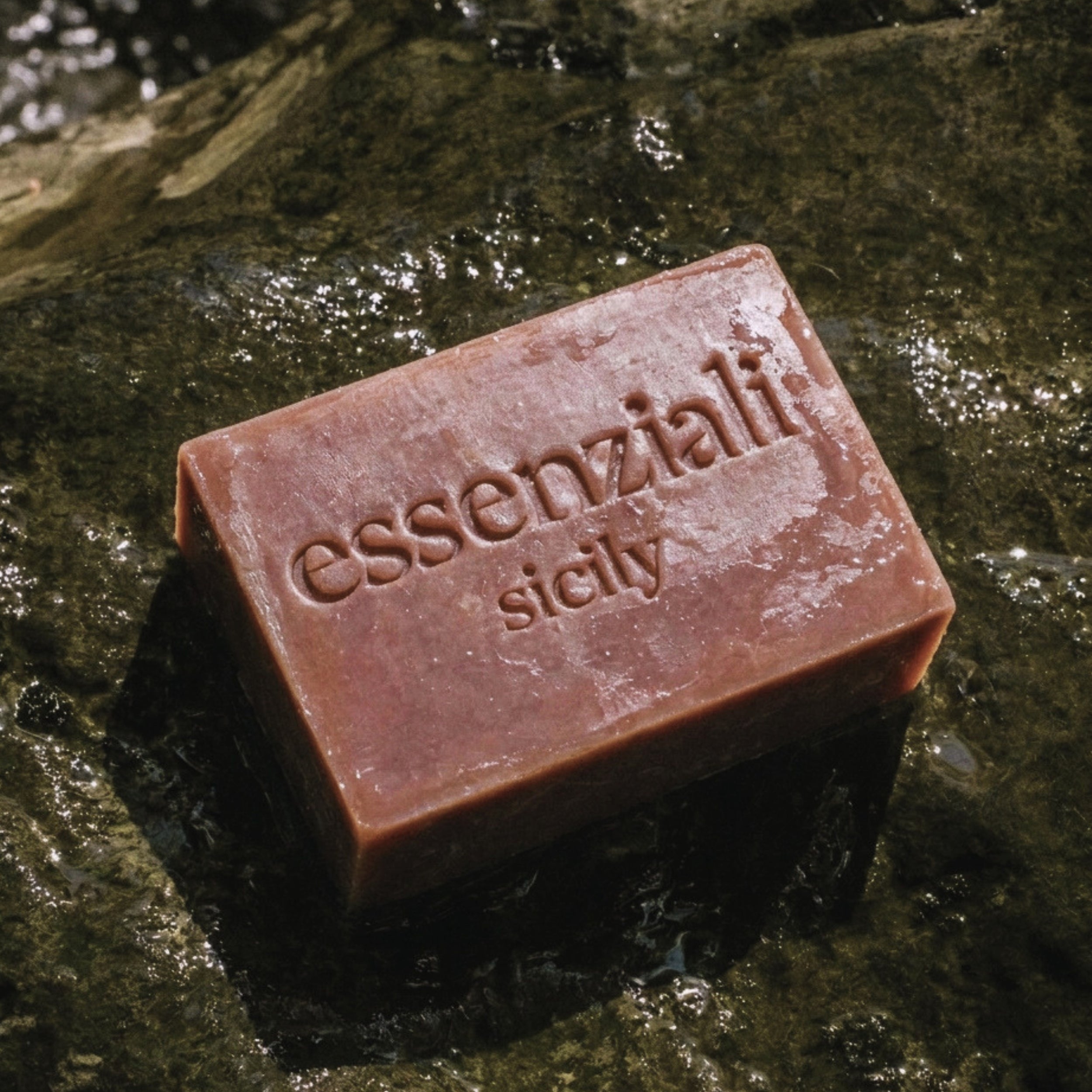 Bar of soap with 'essenziali sicily' branding on a wet stone surface