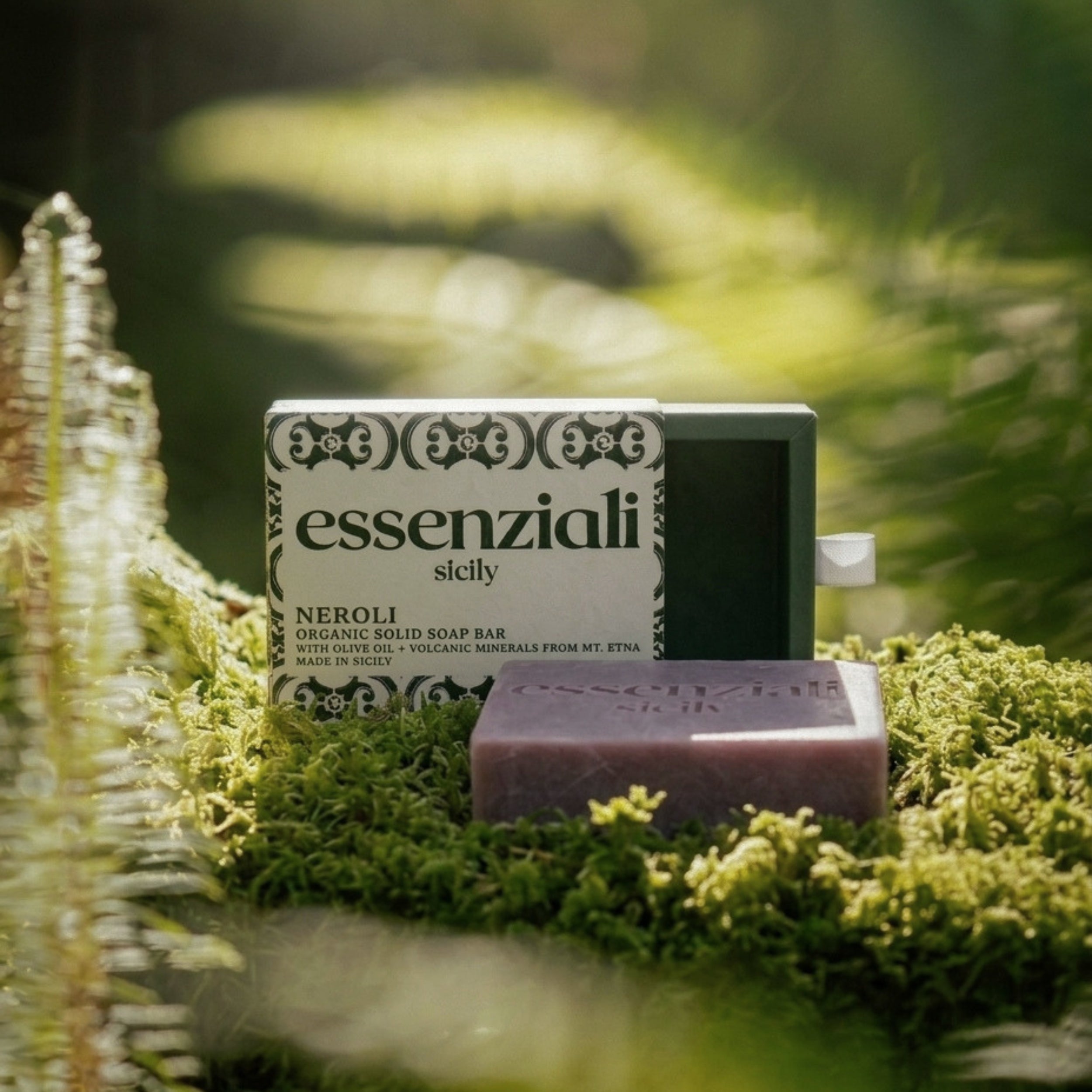 Bar of soap with 'essenziali' packaging on a grassy surface
