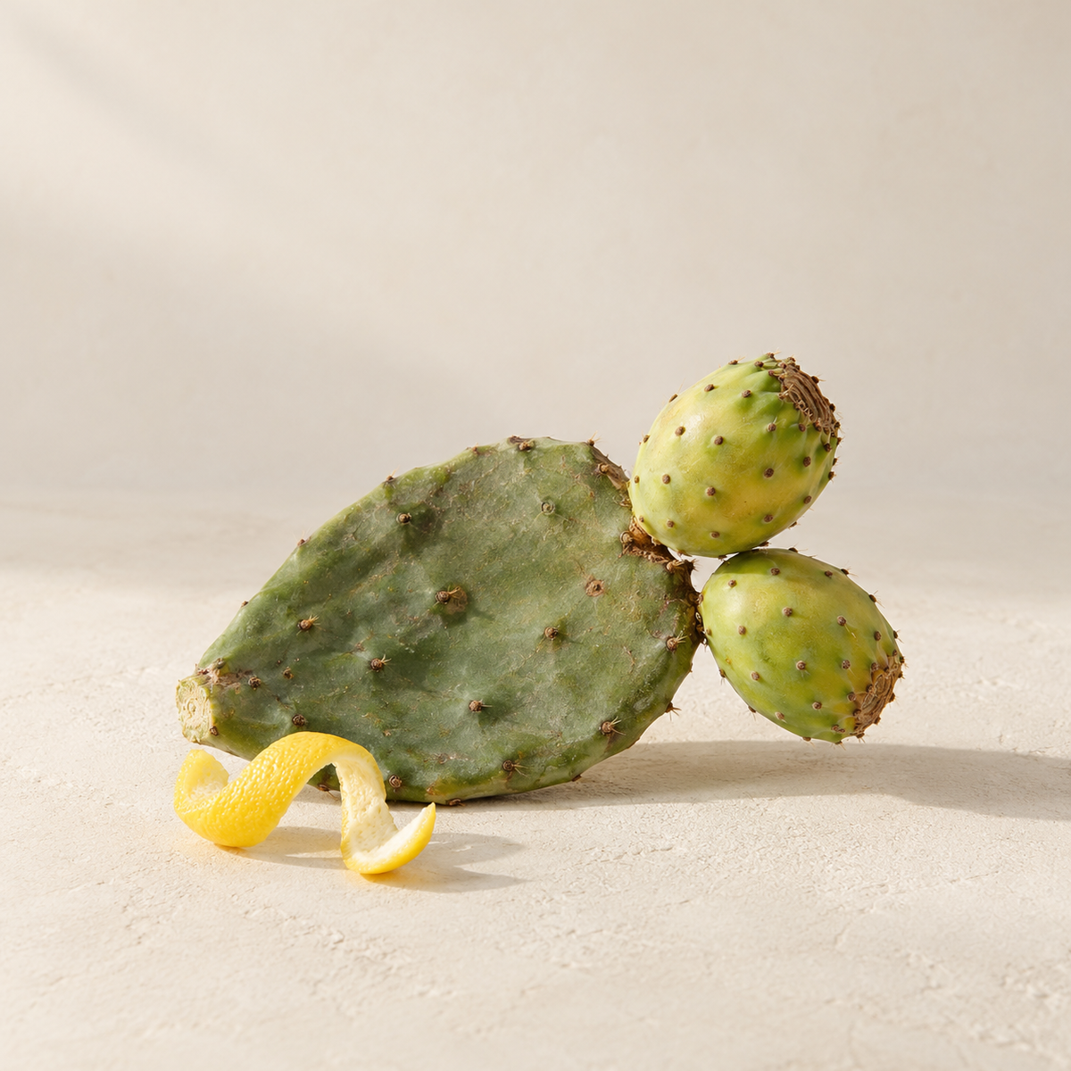 Prickly pear cactus and green fruit with a lemon peel curl on a cream background